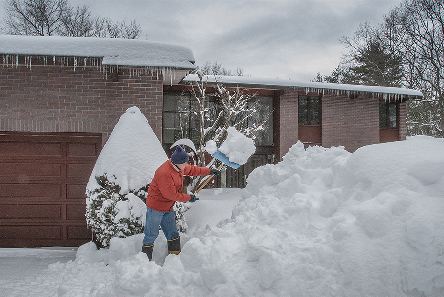 Senior man shoveling snow in front of split level house