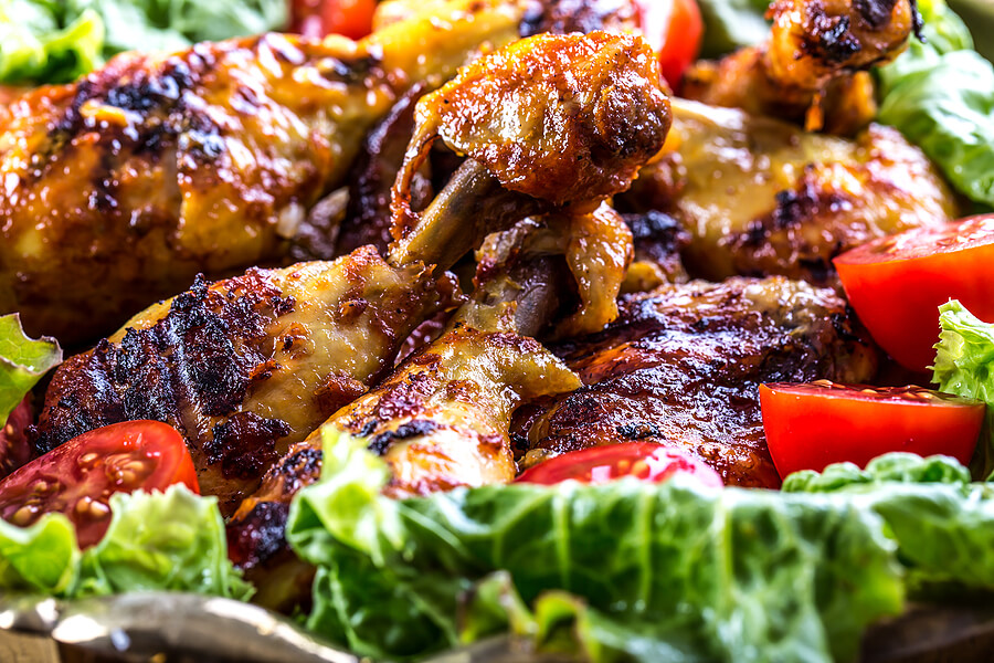 A platter of grilled chicken surrounded by lettuce leaves and sliced cherry tomatoes.