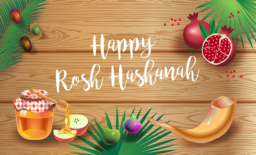 a wooden table with honey, sliced apples, a shofar and the message Happy Rosh Hashana