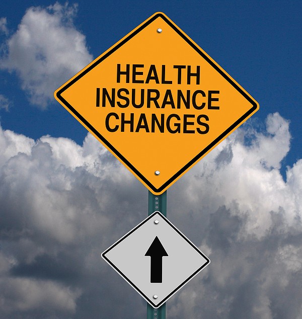 Yellow diamond shaped road sign reading Health Insurance Changes with an arrow indicating changes are ahead against a dark bank of clouds
